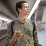 Sustainable Fashion Transition - Young ethnic man in earbuds listening to music while waiting for transport at contemporary subway station