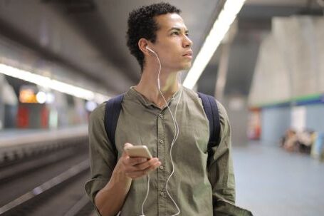 Sustainable Fashion Transition - Young ethnic man in earbuds listening to music while waiting for transport at contemporary subway station
