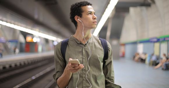 Sustainable Fashion Transition - Young ethnic man in earbuds listening to music while waiting for transport at contemporary subway station