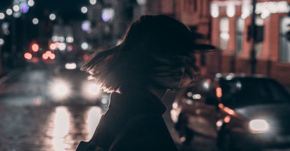 Fashion Movement - Woman in Black Jacket Carrying Backpack With Tousled Hair Walking On The Street At Night