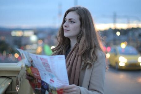 Clothing Exchange Guide - Female traveler in warm clothes standing on street with map and looking away at dusk