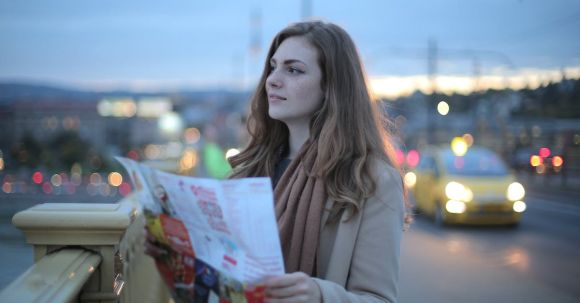 Clothing Exchange Guide - Female traveler in warm clothes standing on street with map and looking away at dusk